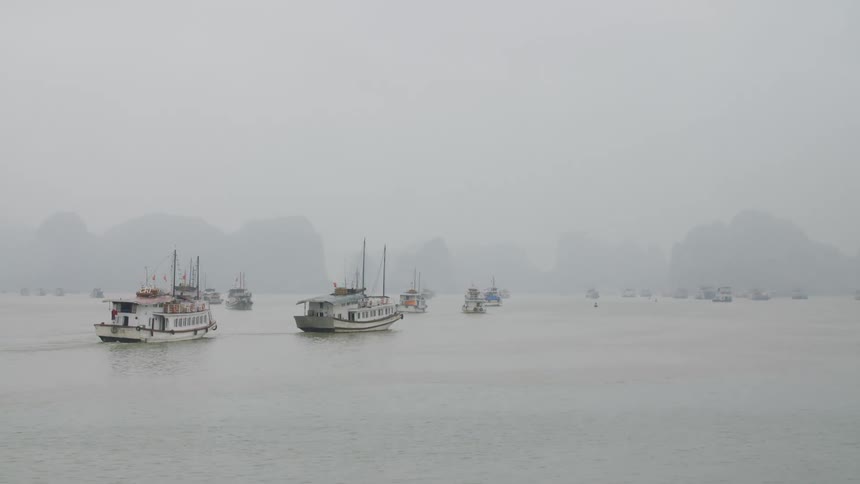 Boats travel across the foggy ocean during the day