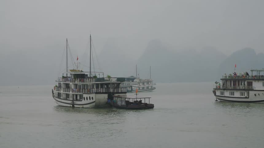 A ship tows a boat behind it across a body of water through thick fog