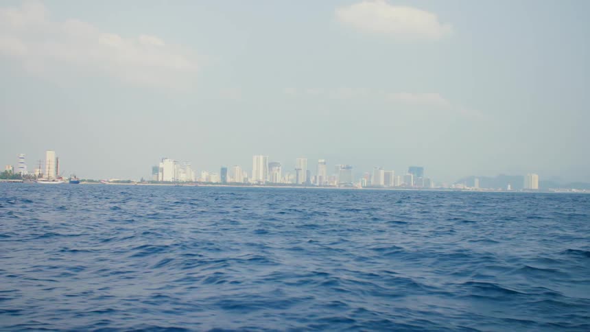 A big city skyline from a distance with high rise buildings on the horizon seen from a boat traveling across the sea