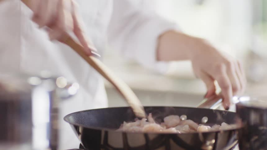 A woman at home adds shrimp to a pan as she cooks