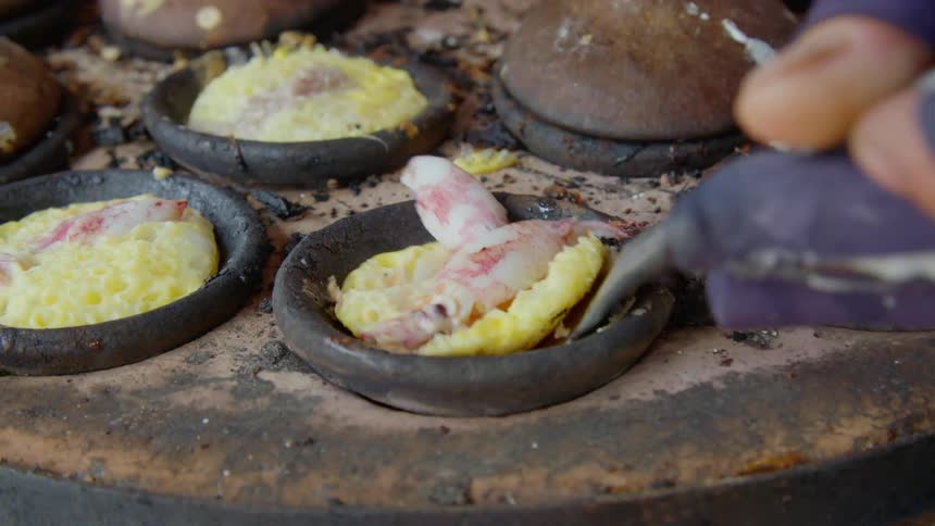 A cook uses a small spatula to scoop shrimp and eggs from a small cooking cup onto a plate