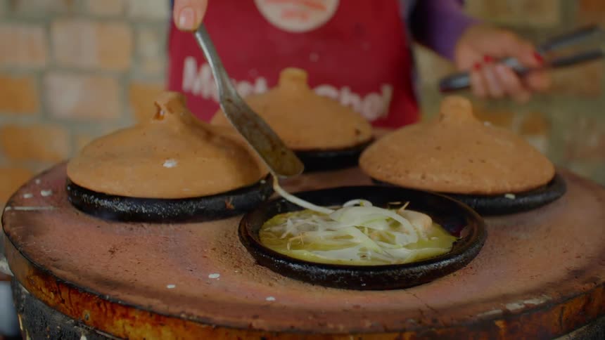 A person cooking and stirring food in cast iron pots