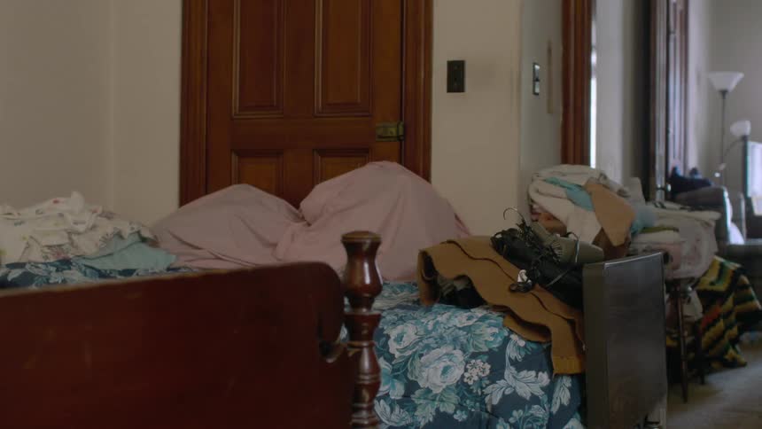 Clothing and items are piled on a bed with a floral cover