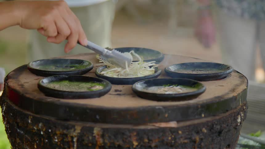 A person cooking a typical regional dish in small black dishes outdoors