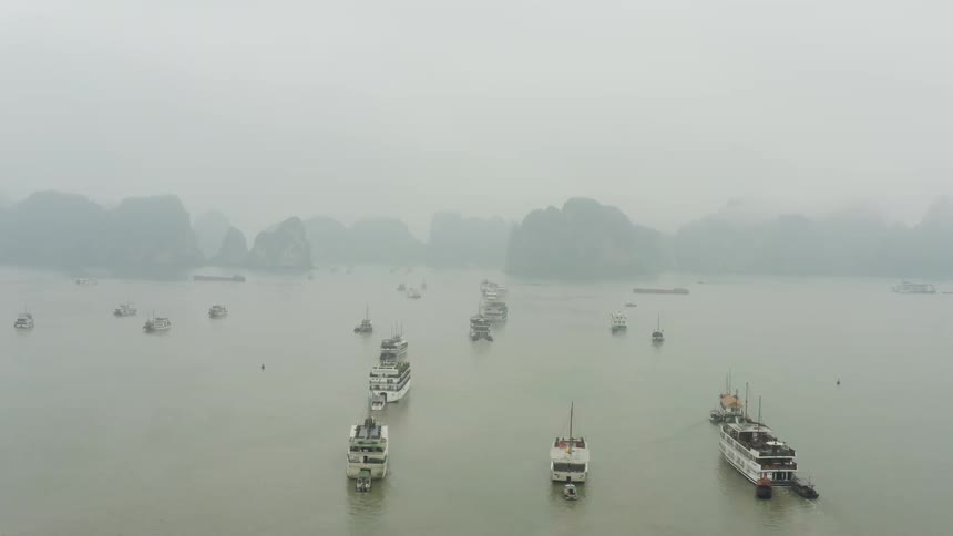 Several boats anchored off a rocky shore in a thick fog