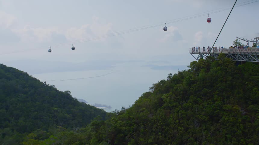 People standing on a platform next to the hills with a gondola lift the sky and clouds in the background