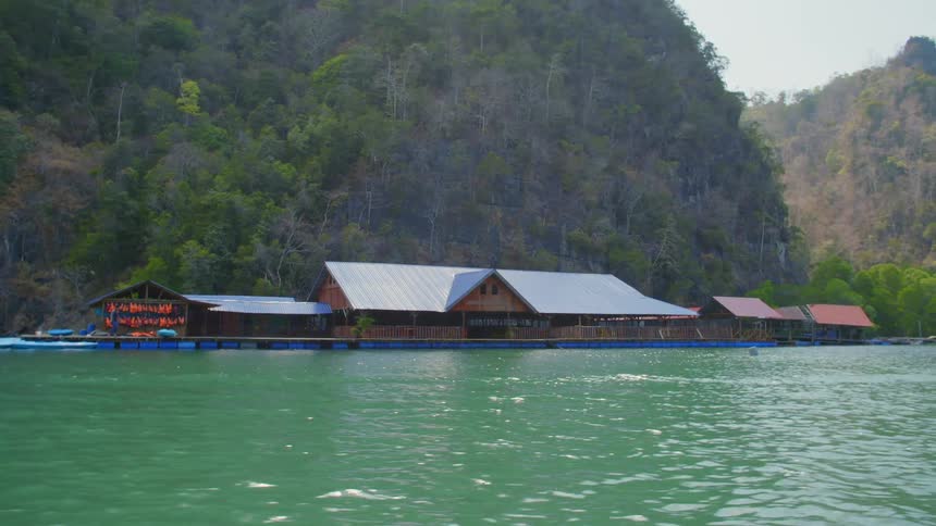 A wooden marina on a blue green ocean at the base of mountain covered in thick vegetation
