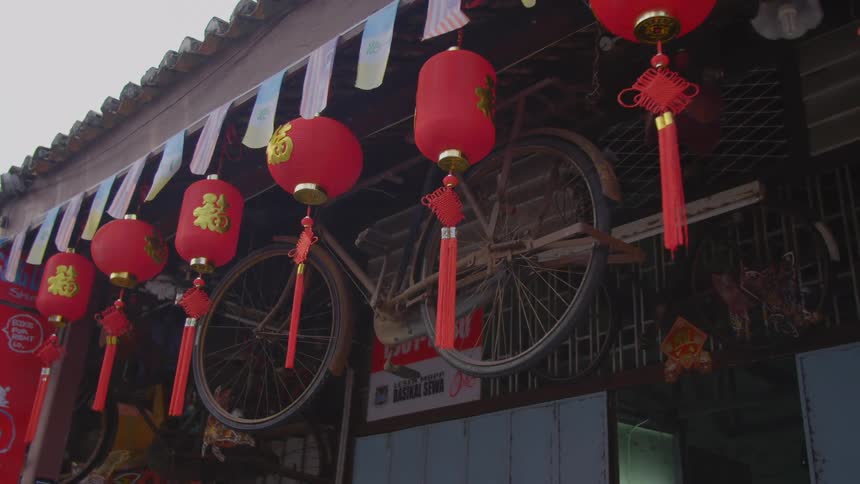 Red chinese lanterns hanging from a building next to a rusty bike