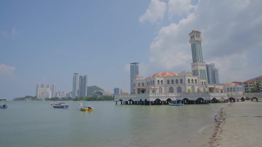 Boats move away from beach and seaside building with city skyscrapers standing near mountain