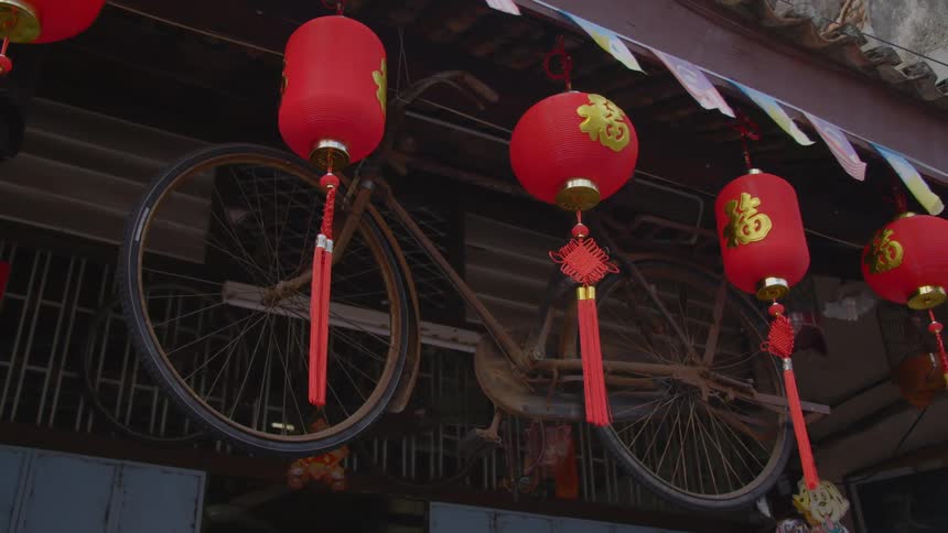 Red chinese lanterns hanging from a building next to a rusty bike