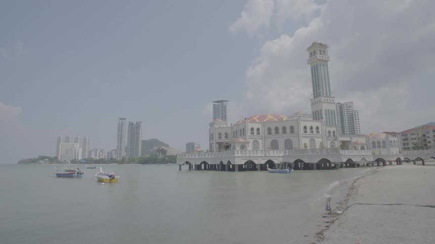 A large building sits on the shore with boats parked by it
