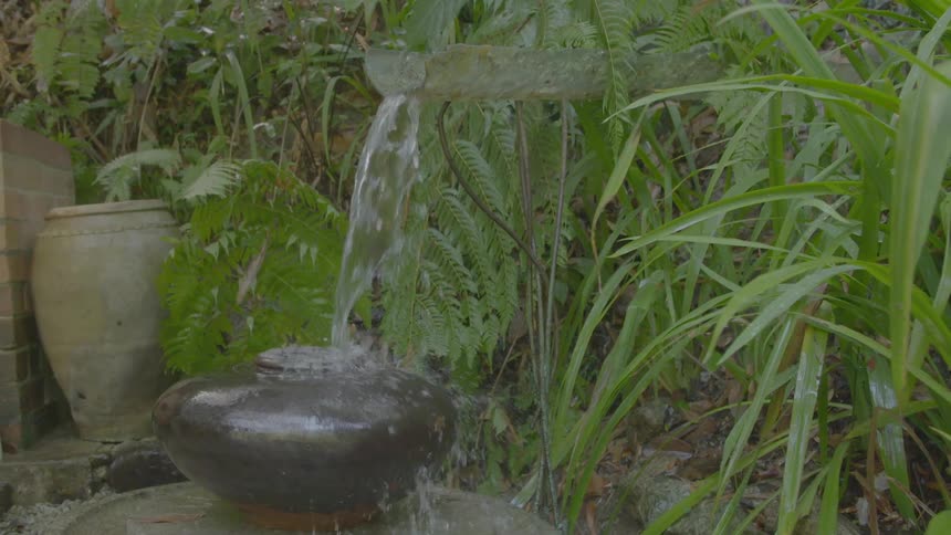 A fountain in a garden fills a pot with water