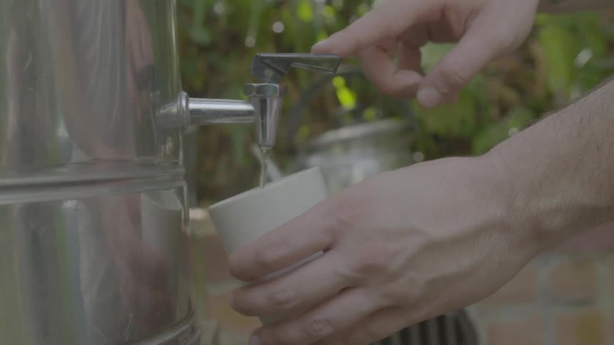 A person holding a cup and getting water from the cooler with plants in the background