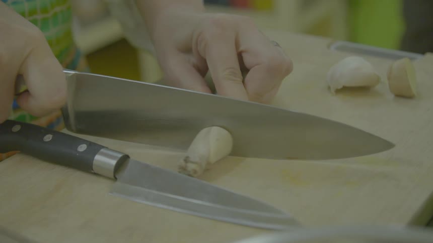 A womans hands holding a knife and cutting food on a cutting board