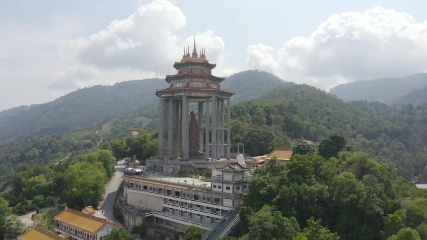 Mist covers mountains on horizon under cloudy sky while statue centered among columns towers over buildings