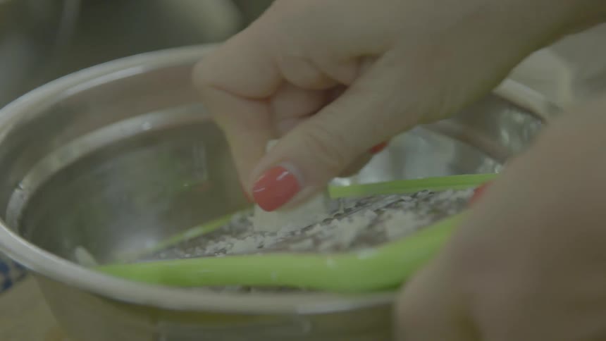 A woman grating cheese into a metal bowl