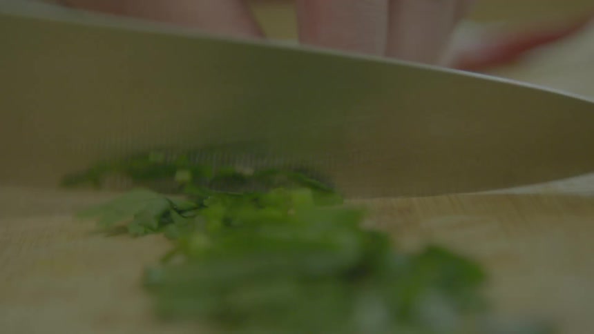A knife cutting leafy herbs on a wood cutting board