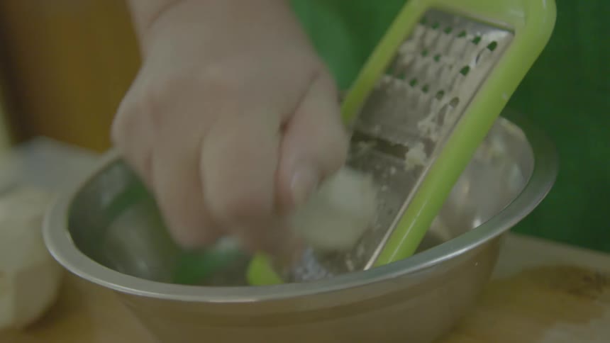 A person using a grater to grate food into a silver bowl on a table