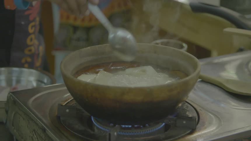 A person cooking a bowl of food on a gas burner