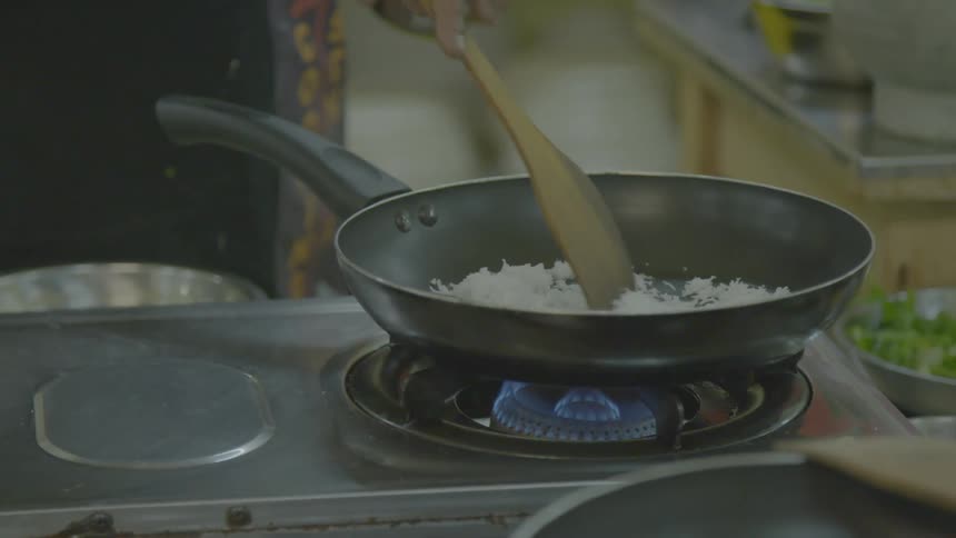 A person stirring food cooking on a stove top with a wood spoon