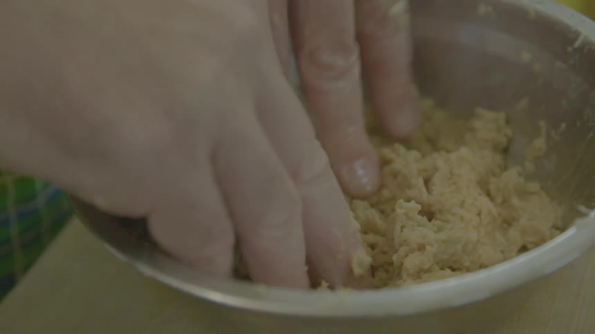 A person kneading food in a metal bowl