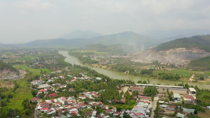 A murky river runs through a small town towards a fog shrouded mountain in the distance