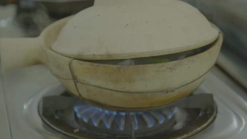 Food emits steam as it cooks in a ceramic pot on a stove top