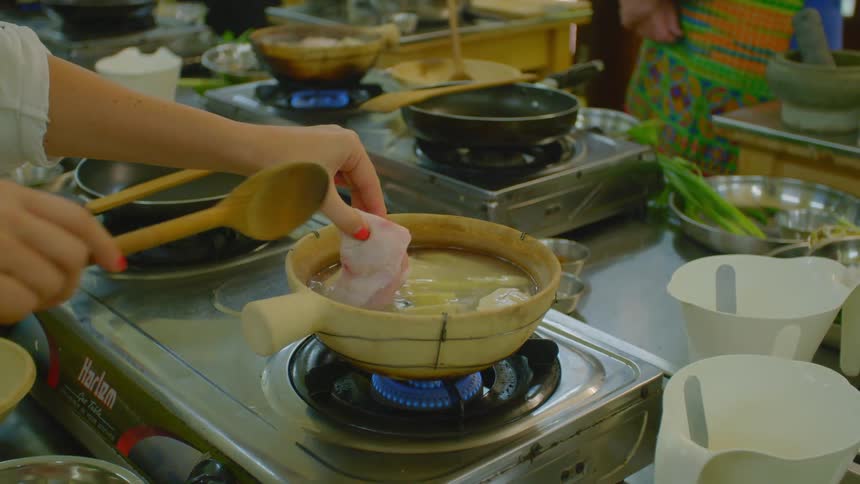 A woman placing food into a boiling pot