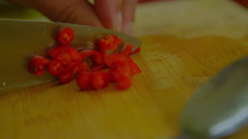 A knife cutting through a red pepper on a wood cutting board