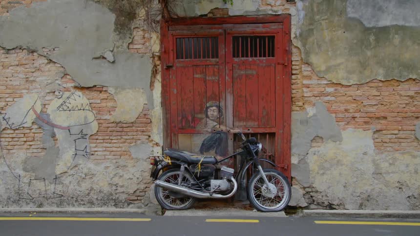 A motorcycle sits against a red door with artwork of a crouching man and creates the illusion that hes riding it