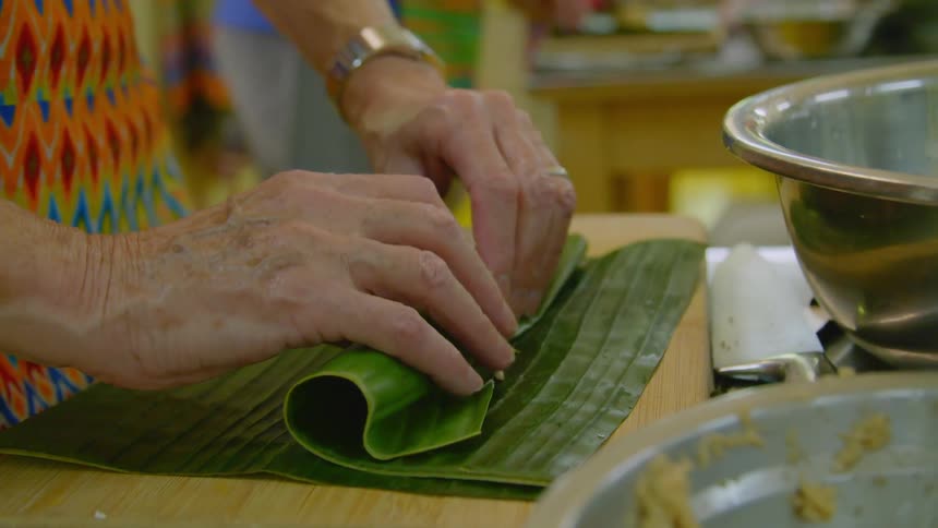 A woman rolls a banana leaf with yellow filling inside