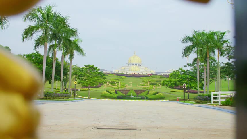 A gold gate in front of a palace and gardens on a summer day