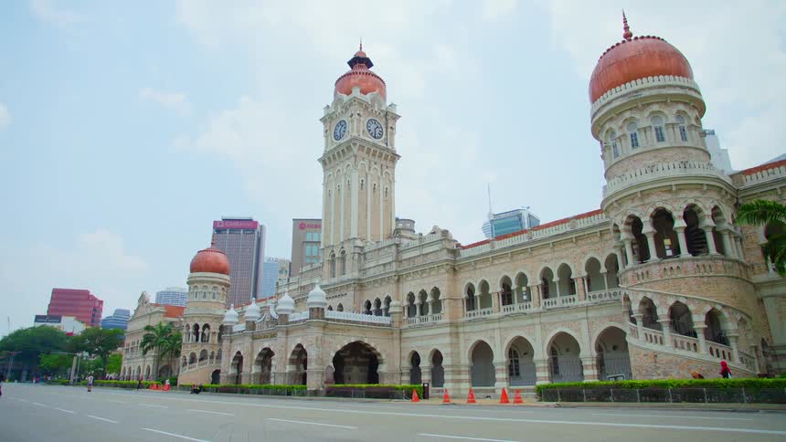 A building with arches and a clock tower with the sky and clouds in the background