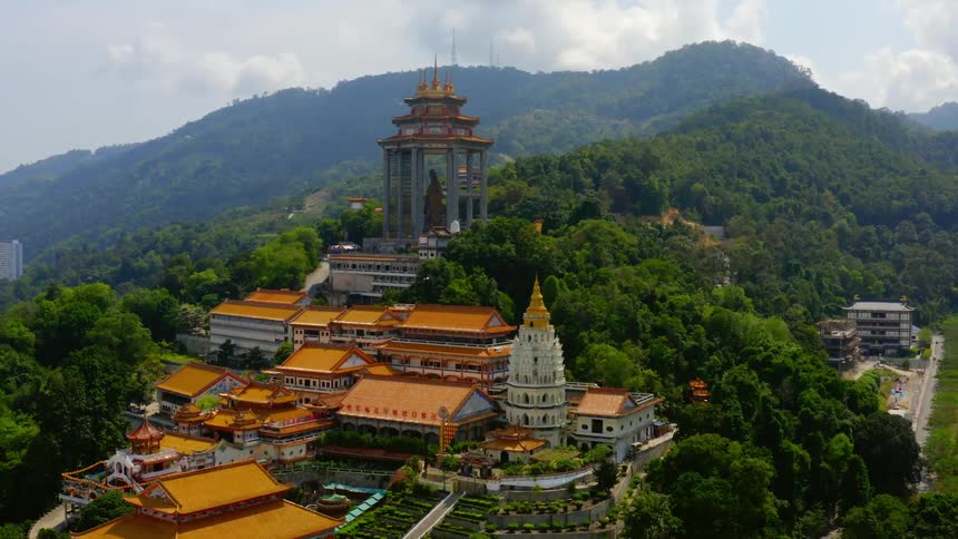 A temple is located atop a forested mountain and surrounded by many buildings