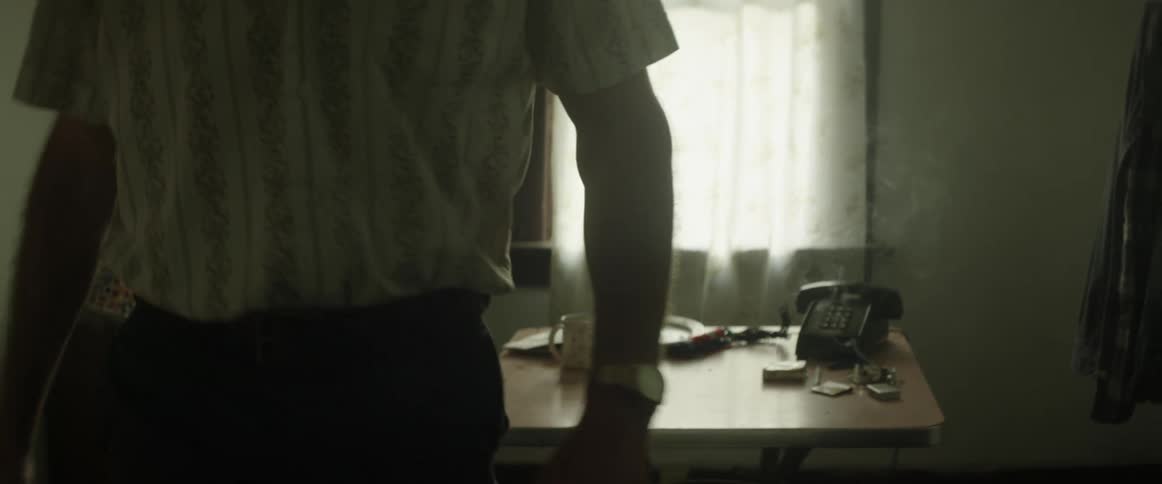 A man in a room with a table and a phone placing a gun in his waistband
