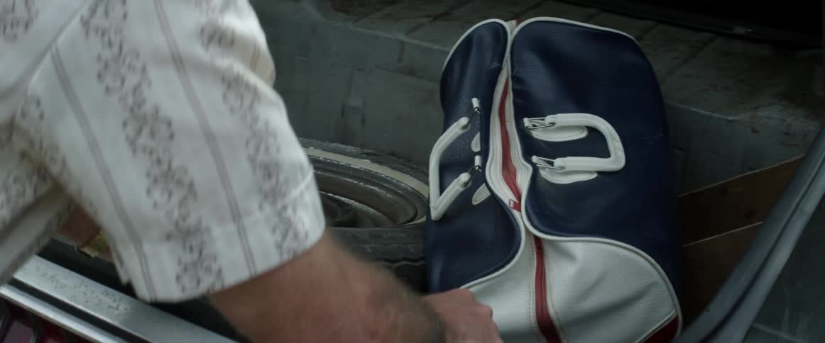 A man looking into a car trunk with a spare tire and a bag