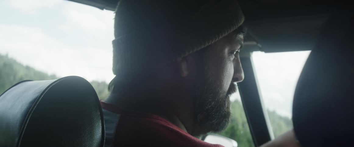 A man driving his car looks towards the passenger seat and talks
