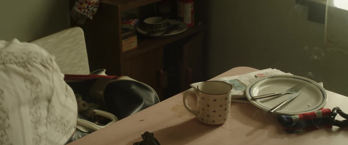 A man sitting at a table with a coffee mug and empty plate puts a map in a bag and jumps up