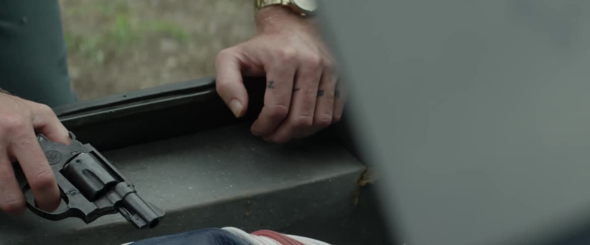 A man holds a small handgun as he stands over a large box outside with the lid open