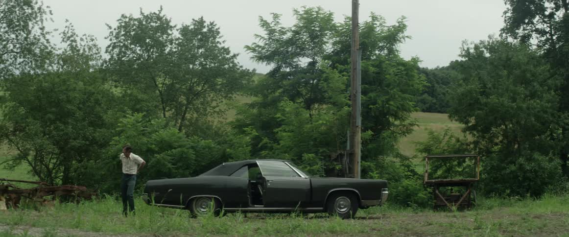 A man is in a rural area next to his parked car