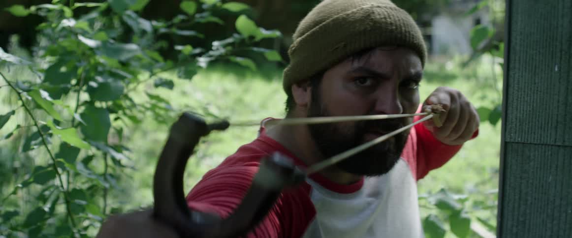 Man wearing a beanie shoots a slingshot in the backyard