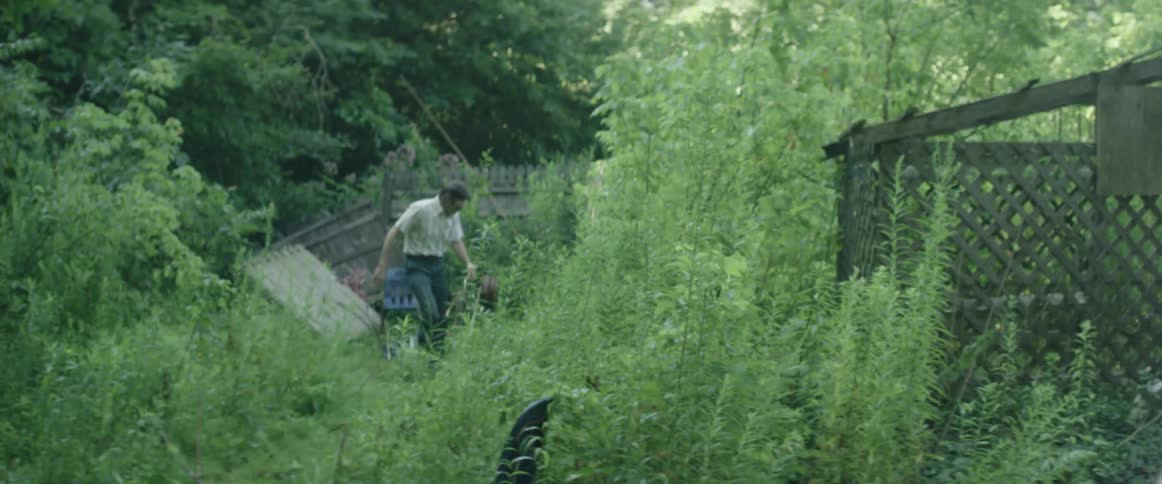 A man carrying a slingshot searches for something on the overgrown backyard