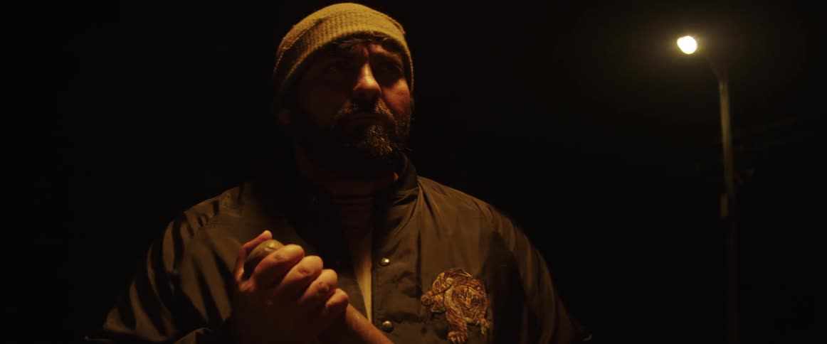 A man gripping a baseball bat outside at night with an angry look on his face