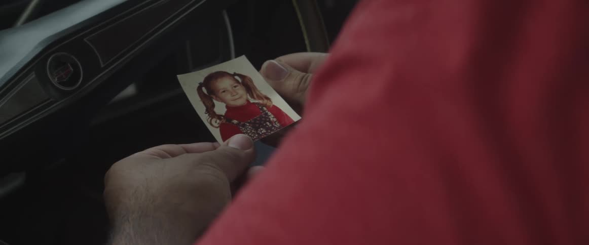 Man sitting in the driver seat of a car contemplates a picture of a little girl