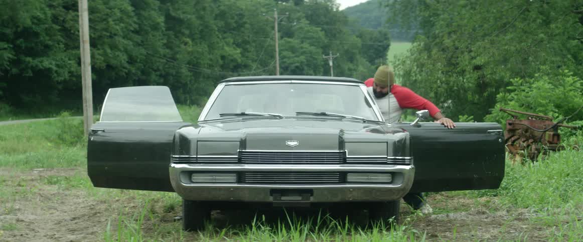 A man has his car parked in a rural area