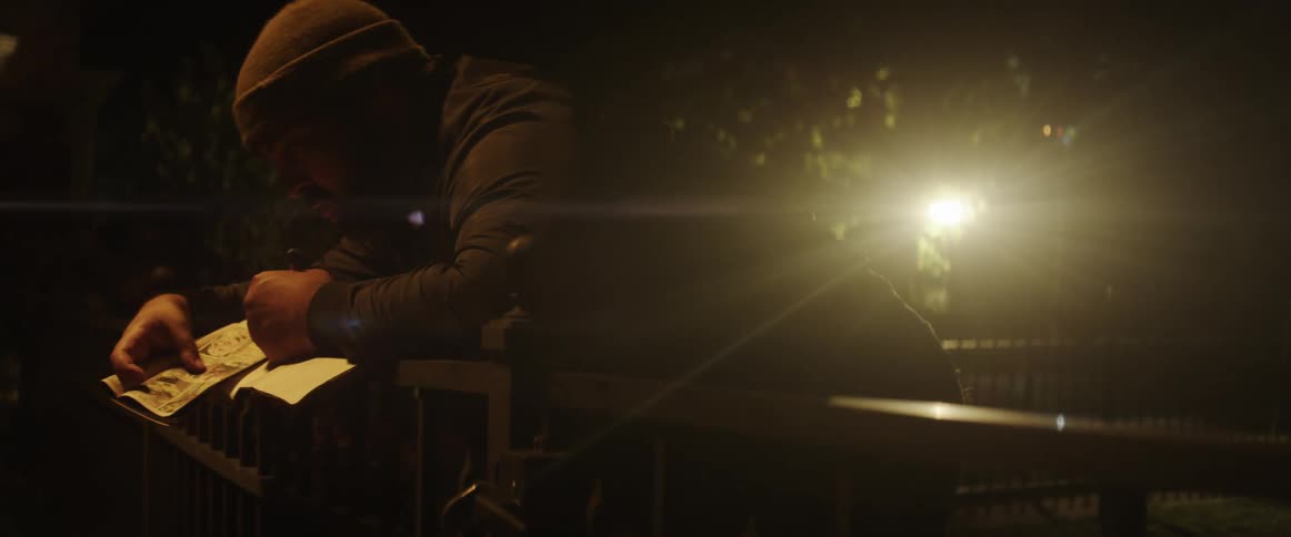 Man copies drawings on paper reclined on a railing in a public park at night