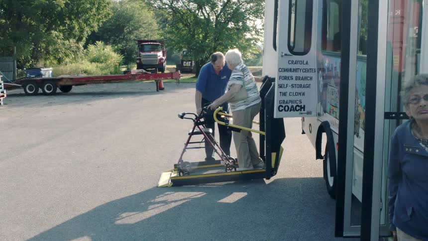 A bus driver lowering a woman from a bus with a wheelchair lift