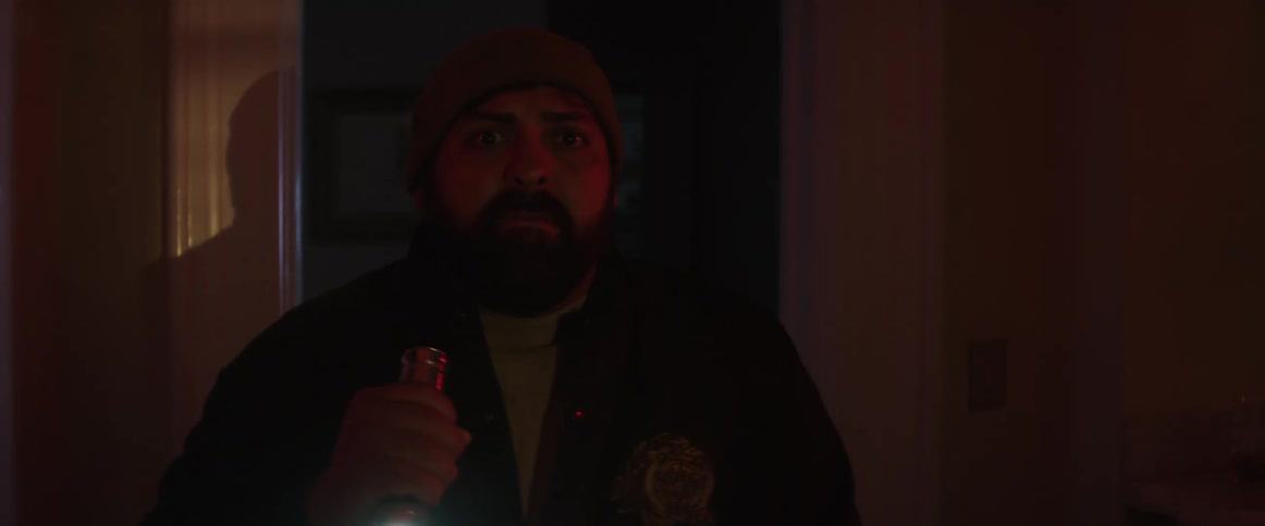 A man with a hat and a flashlight walking through a doorway and pointing a gun