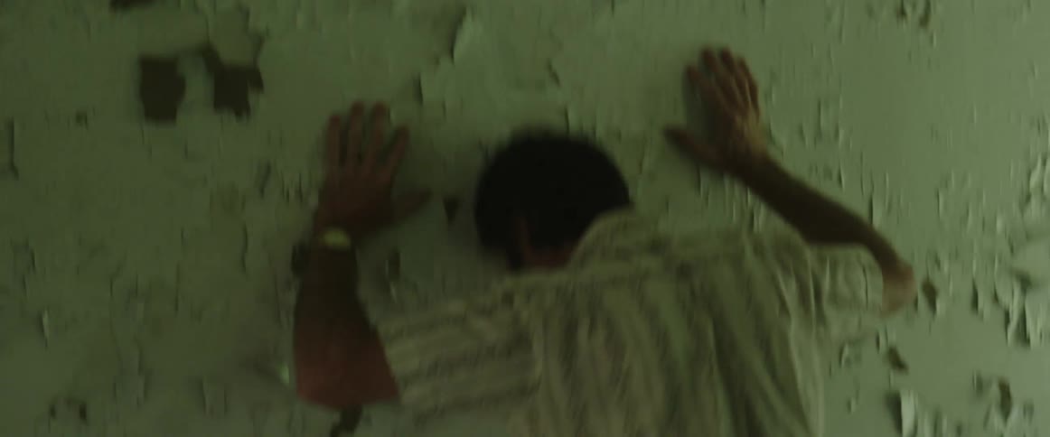 Two men argue in a run down house as one man throws himself against the wall in frustration