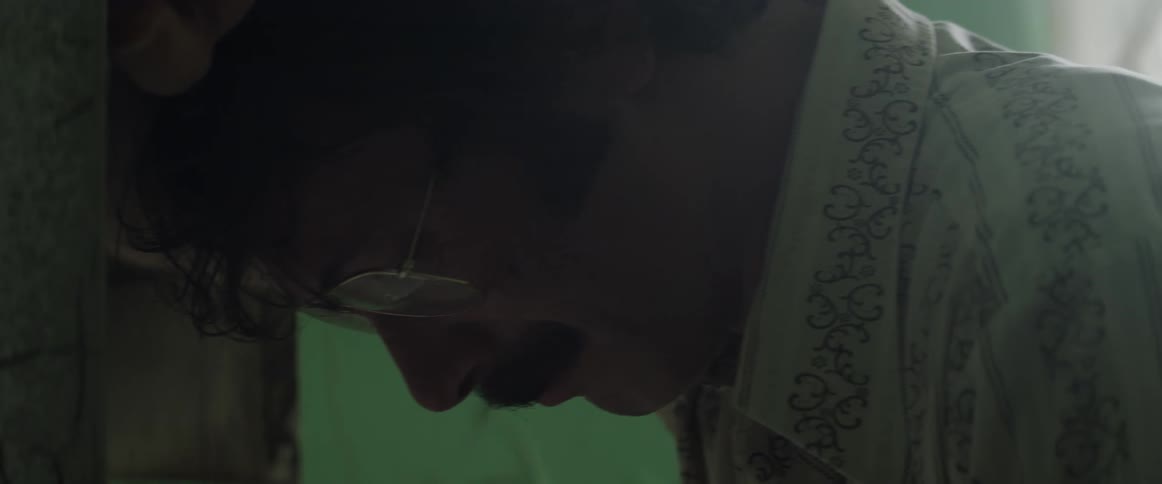 A man with glasses putting his head against the wall with a window in the background